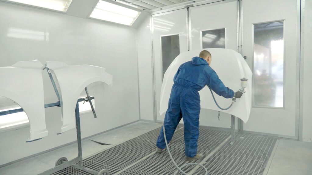 auto painter spraying white paint on car hood in special booth